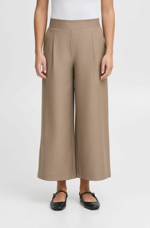 Brown wide-leg trousers made from a smooth fabric. Features pleats at the front and a high waistband. Worn with black flats.