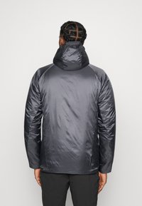 Dunkelgraue Daunenjacke mit hohem Kragen und Kapuze, die eine glatte, glänzende Textur aufweist. Sie ist mit Raglanärmeln ausgestattet und hat keine sichtbaren Beschläge.