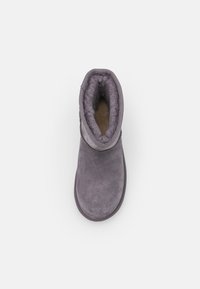 Bottine grise en daim avec une doublure douce et texturée. La bottine a un bout arrondi et une semelle plate, avec un revers pliable en haut.