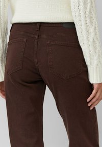 Jean en denim marron avec une taille ajustée, deux poches arrière et une texture subtile. Associé à un pull en tricot crème.