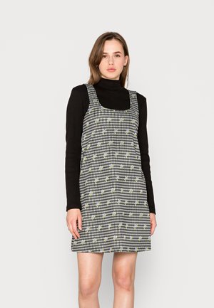 Vestido quadriculado em preto e branco com padrões florais, decote quadrado e alças largas, combinado com uma blusa preta de mangas compridas.