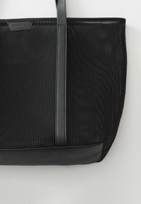 Zwarte totebag met een gaasontwerp, voorzien van een glad leren bodem en handvatten. Het hexagonale patroon op het gaas zorgt voor een gestructureerde uitstraling.