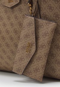 Hnědá texturovaná kabelka s vzorem loga, zlatými akcenty loga a připojenou odpovídající peněženkou. Má strukturovaný tvar a dva popruhy.
