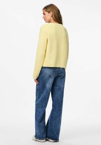 Dzeltena ribota džemperis ar saīsinātu dizainu. Apvienots ar brīvu zilu džinsu stilu. Gaisma auduma tekstūra un vienkārša forma.
