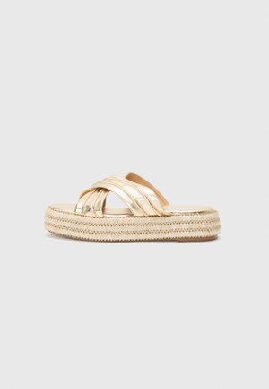 Metallic gold platform sandals with crisscross straps and a textured rope sole. Smooth upper material, flat design, and open toe.