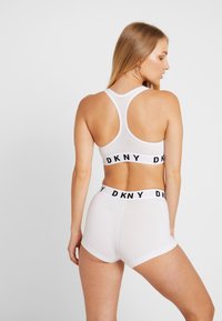 Bijela sportska grudnjak i kratke hlače s elastičnim trakama s DKNY logom. Glatka tkanina, dizajn s leđa i uski kroj.