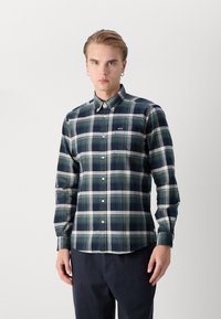 Kockás ing tengerészkék, fehér és Türkiz kockás mintával, gombos gallérral, hosszú ujjakkal, és egy logóval ellátott zsebbel.