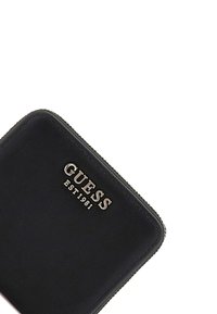 Černá kožená peněženka s vyraženým stříbrným logem "GUESS" a nápisem "EST 1981." Disponuje hladkým povrchem a zipovým uzávěrem na horním okraji.