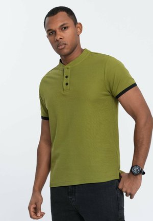 Camisa polo verde oliva con textura acanalada, ribete negro en las mangas y el cuello, tres botones negros en la tapeta. Jeans oscuros.