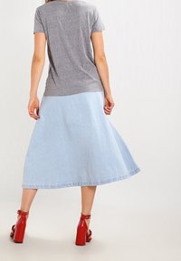 Grå kortærmet T-shirt, parret med en lys blå denim midi-nederdel. Har en let og flowy stof og røde højhælede sandaler.