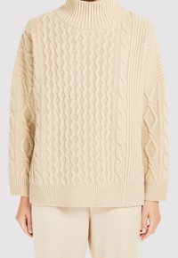 Beige neulepaita korkealla kauluksella, jossa on teksturoitu palmikkokuvio ja resorit hihansuissa ja helmassa. Pehmeä, mukava ja väljä istuvuus.