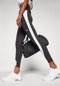 Leggings neri con strisce laterali bianche, con logo Puma sulla sinistra. Abbinati a scarpe da ginnastica bianche e a una borsa da palestra nera.