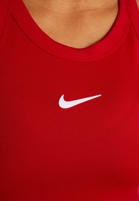 Débardeur de sport rouge en tissu texturé et respirant. Présente un logo Nike blanc centré sur la poitrine. Coutures plates et encolure ronde.