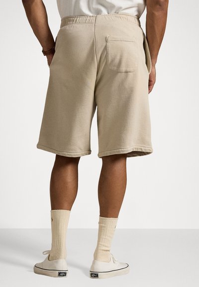 Shorts en coton beige avec une taille élastique, des poches latérales et une poche arrière. Les jambes sont de longueur genou avec des ourlets cousus.