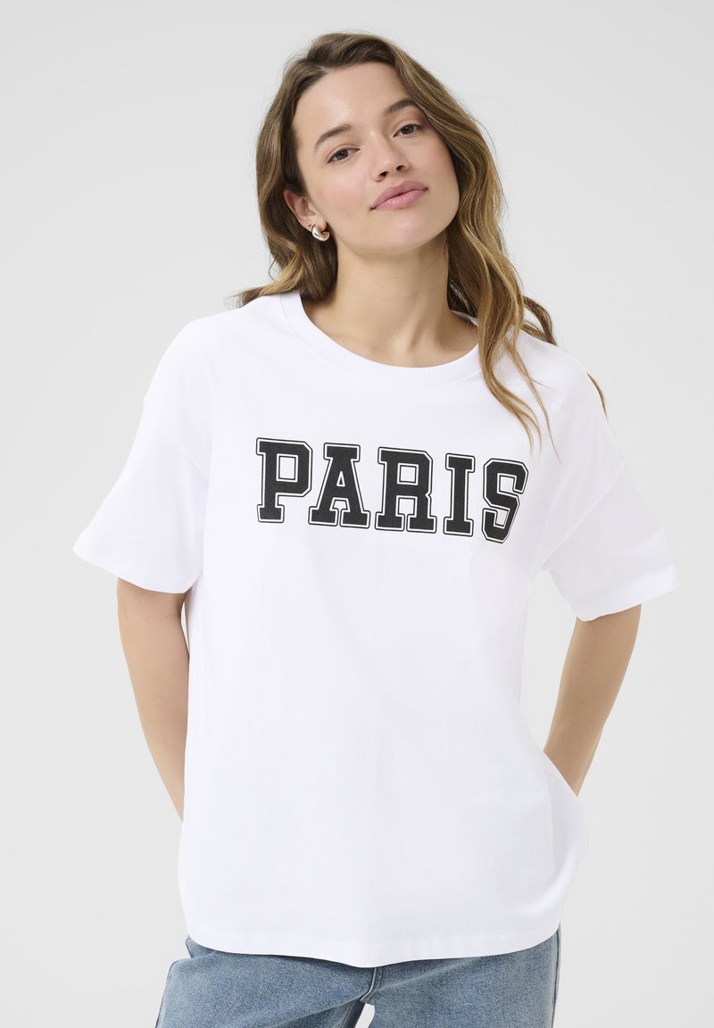T-shirt en coton blanc avec un texte noir en gras disant "PARIS". Coupe décontractée, manches courtes et encolure ronde.