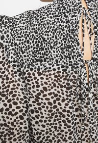 Svart och vit blus med smockdesign, prydd med ett prickigt mönster, volangärmar och öppen rygg med band och dekorativa pärlor.