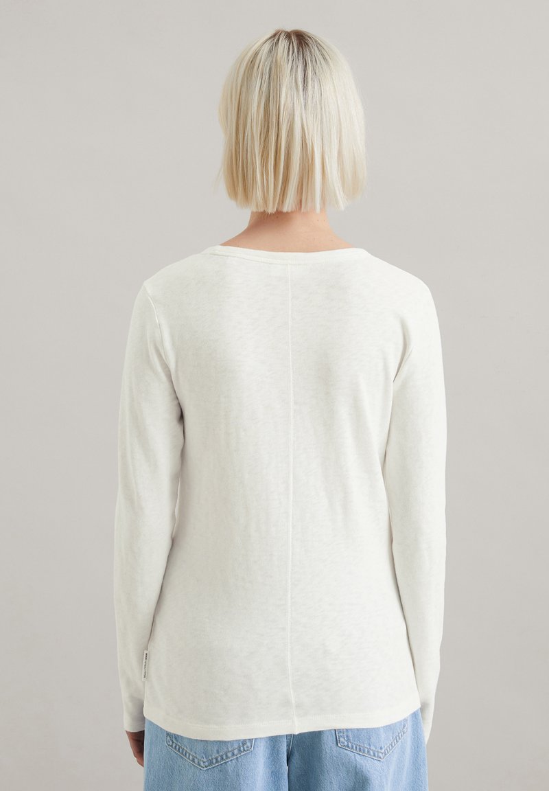 Długi rękaw, kremowy top wykonany z miękkiej, teksturowanej tkaniny. Posiada okrągły dekolt oraz prosty szew na plecach z widocznym szyciem.