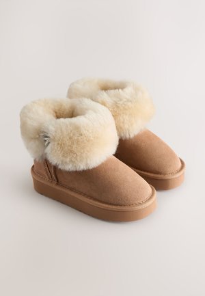 Beżowe botki ze skóry zamszowej z grubym kremowym mankietem z futra syntetycznego i gumową podeszwą, o gładkiej konstrukcji i zaokrąglonym nosku.