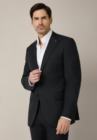 Czarny dopasowany garnitur z klapami typu notch, z zapięciem na jeden guzik i dwoma przednimi kieszeniami, noszony na białej koszuli.