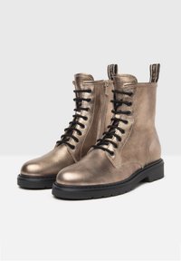 Bottines en bronze métallique avec une texture lisse, lacets noirs, fermeture éclair latérale et semelle noire robuste. Équipées d'anses pour un enfilage facile.