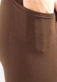 Leggings da allenamento marroni con una texture liscia, dotati di una tasca laterale e dettagli di cuciture a contrasto; pannello in mesh traspirante sulla parte inferiore della gamba.