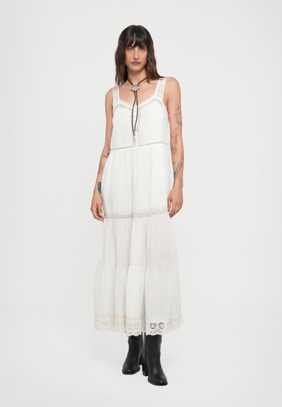 Vestido maxi blanco con borde de encaje, diseño en capas y una textura ligera. Combinado con botas negras hasta la rodilla, que cuentan con lazos ajustables en el escote.
