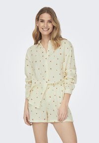 Ensemble chemise à manches courtes et short de couleur jaune clair, ornée de petits motifs floraux rouges. Fabriqué en tissu doux et texturé avec une coupe décontractée.
