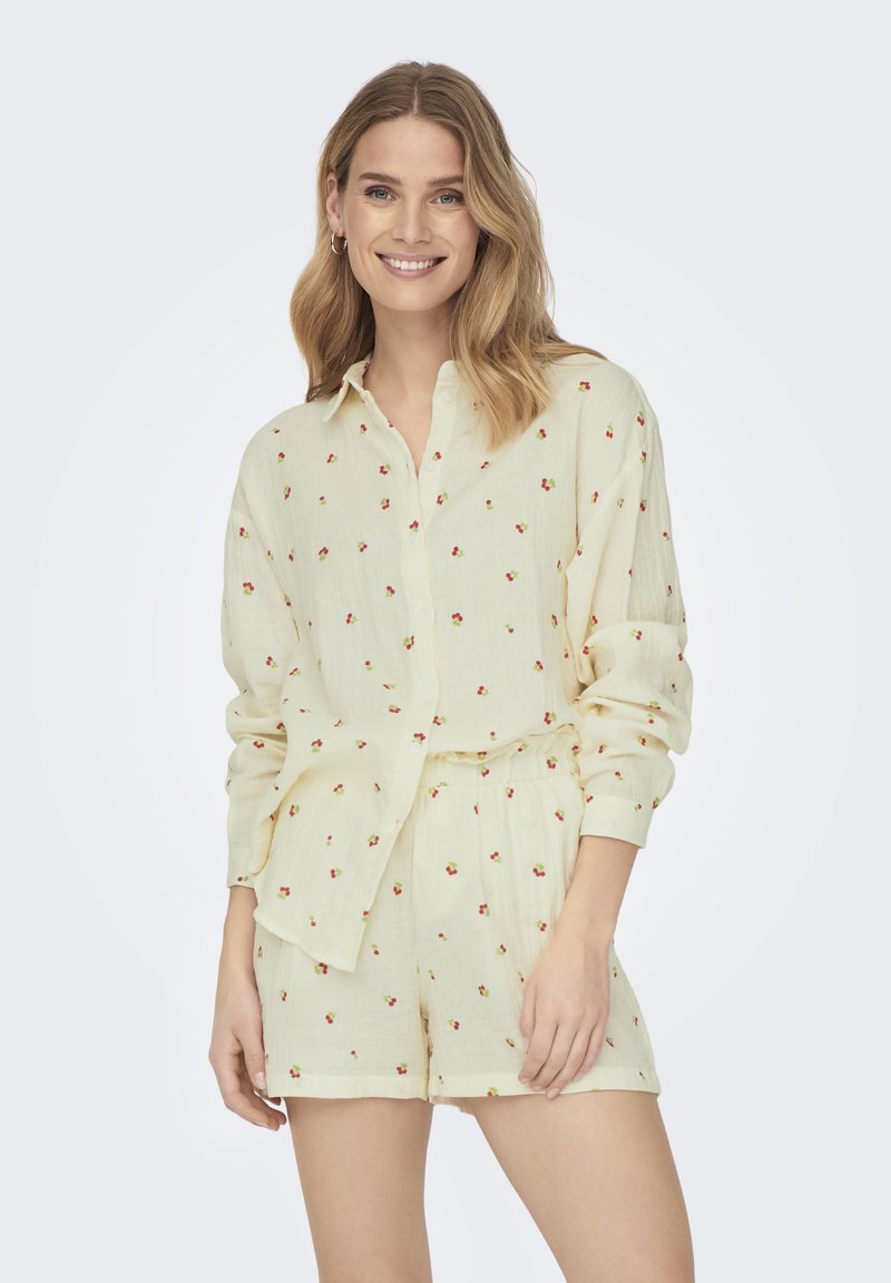 Ensemble chemise à manches courtes et short de couleur jaune clair, ornée de petits motifs floraux rouges. Fabriqué en tissu doux et texturé avec une coupe décontractée.