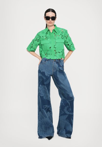 Green floral cut-out cropped shirt with two front pockets, paired with wide-leg denim pants featuring a blue floral pattern and pointed black heels.