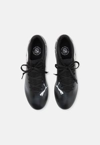 Zapatillas deportivas negras con parte superior de malla texturizada, detalles blancos y cordones negros, con una forma distintiva y un diseño elegante.