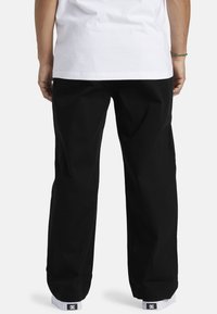Black pants with a loose fit and straight legs, featuring a smooth texture. Worn with white shoes and a plain white t-shirt.