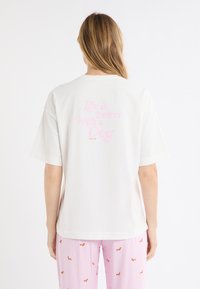 Maglietta bianca in cotone con maniche corte, con scritta rosa sul retro: "La vita è migliore con un cane." Design semplice con scollo rotondo.