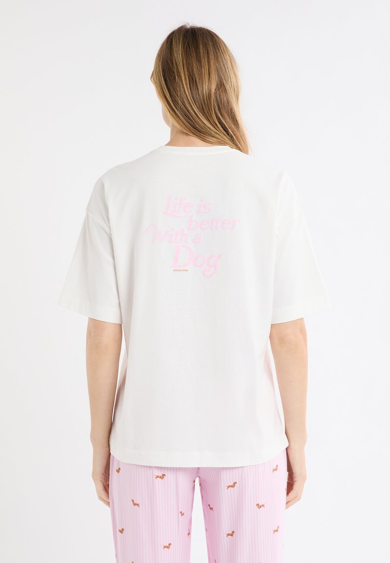 Maglietta bianca in cotone con maniche corte, con scritta rosa sul retro: "La vita è migliore con un cane." Design semplice con scollo rotondo.