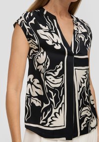 Schwarzes ärmelloses Oberteil mit cremefarbigem Blumenmuster, das einen V-Ausschnitt und einen lockeren Schnitt hat. Glattes Material mit einer leicht glanzmäßigen Textur.