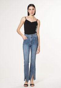 Jeans blu a vita alta con orli sfalsati, dotati di tasche frontali e chiusura con bottone. Abbinati a un top canotta nero.