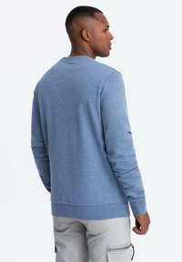 Svetr s kulatým výstřihem ve světle modré barvě, vyrobený z měkké tkaniny. Má žebrované manžety a spodní lem. Jednoduchý design s hladkou texturou, bez vzorů nebo akcentů.