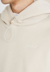 Beige hettegenser laget av myk fleece med snor lukking og brodert "Levi's" logo i subtil tone-i-tone søm.