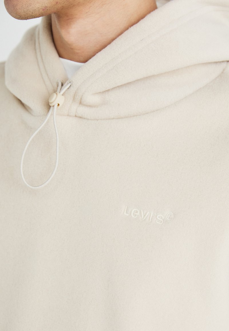 Felpa con cappuccio beige in morbido pile, dotata di chiusura con coulisse e logo ricamato "Levi's" in cuciture tono su tono discrete.