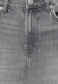 Gros plan sur l'avant d'un jean en denim gris avec bouton fermé et coutures visibles sur la braguette et les poches.