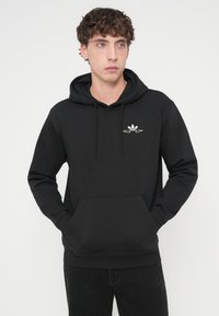 Sweat à capuche noir avec poche avant, cordons de serrage et petit logo blanc sur la poitrine ; texture lisse et coupe décontractée.