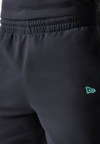 Μαύρο παντελόνι jogger από μαλακό ύφασμα, με ελαστική μέση και μικρό τιρκουάζ λογότυπο στον μηρό για την επωνυμία.