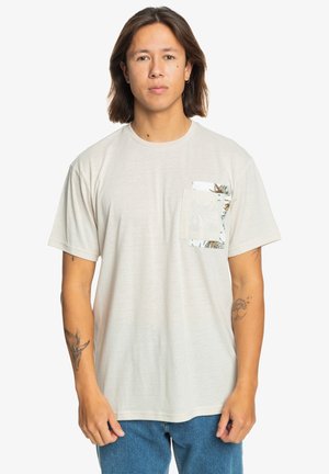 Beige t-shirt with a round neck, short sleeves, and a floral-patterned pocket on the left side. Casual fit made from soft fabric.