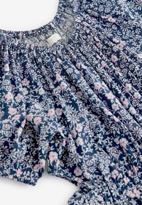 Blouse fleurie avec un fond bleu marine orné de fleurs roses et blanches, col et manches plissés, confectionnée dans un tissu léger.