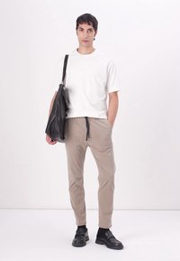 Cămașă albă cu mânecă scurtă texturată, pantaloni bej tapered cu șnur, geantă neagră de umăr și pantofi negri slip-on pe un fundal alb.