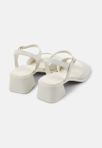 White block-heeled sandals with a wide toe strap and two narrow adjustable ankle straps. Smooth texture, minimalistic design.
