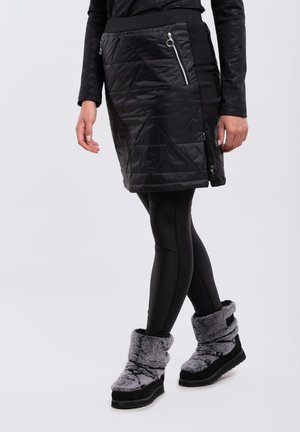 Falda negra acolchada con bolsillos laterales con cremallera, combinada con leggings negros y botas de tobillo de piel sintética gris. Textura suave y diseño ajustado.