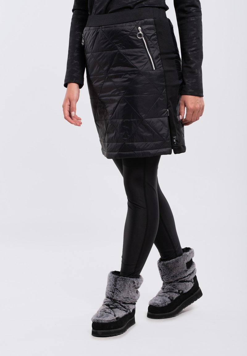 Svart quiltad kjol med sidofickor, i kombination med svarta leggings och grå plyschstövlar vid anklarna. Slät textur och åtsittande design.