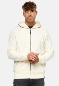 Crème kleurige hoodie met een contrasterende, gemusterde voering in de kap, zakken opzij en geribde manchetten. Bevat een subtiele logo op de borst.