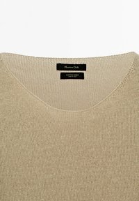 Pull en coton-lin beige tricoté avec un col en V. Présente un tissage texturé et une étiquette de marque bien visible au niveau du col. Fabriqué en Italie.