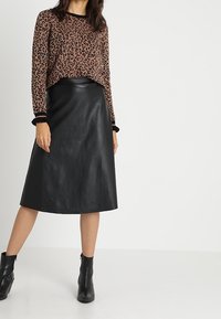 Brun leopardmönstrad tröja med svarta detaljer, i kombination med en svart läder A-linje kjol och anklarboots. Släta texturer och avslappnad passform.